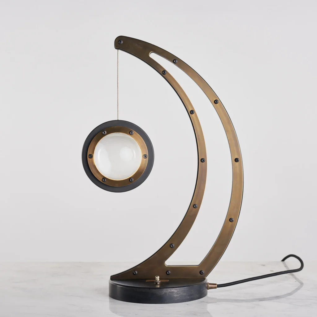 Da Vinci Infinity 1519 table lamp with setting-sun form, genuine brass details, and suspended illuminated capsule. Designed and manufactured by Karice.