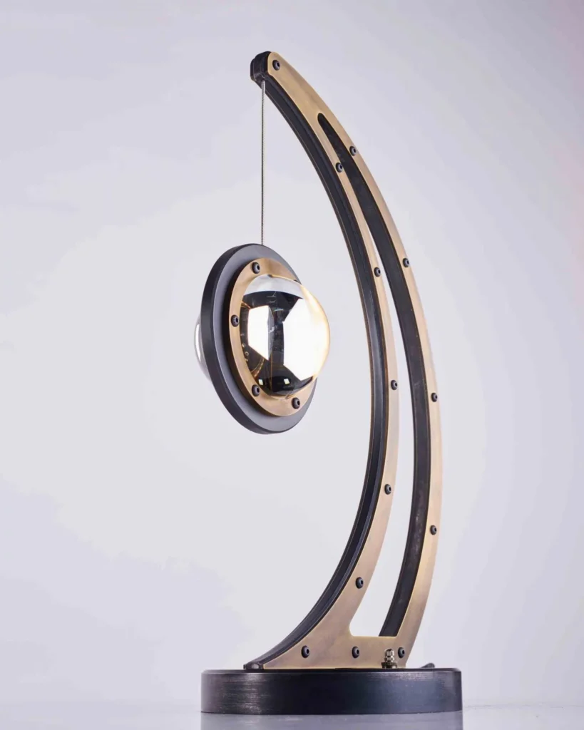 Da Vinci Infinity 1519 table lamp with setting-sun form, genuine brass details, and suspended illuminated capsule. Designed and manufactured by Karice.