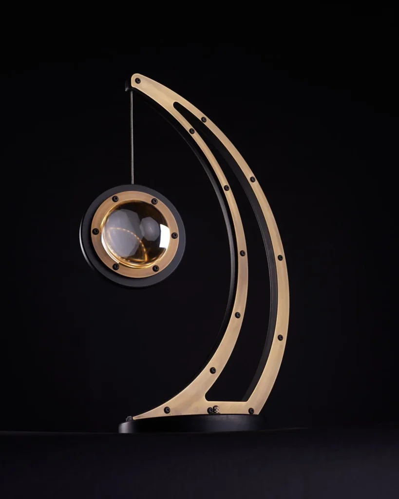 Da Vinci Infinity 1519 table lamp with setting-sun form, genuine brass details, and suspended illuminated capsule. Designed and manufactured by Karice.