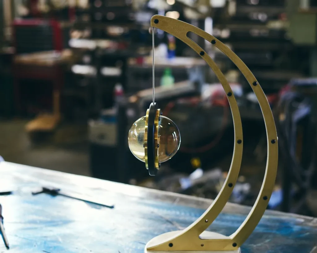 Da Vinci Infinity 1519 table lamp with setting-sun form, genuine brass details, and suspended illuminated capsule. Designed and manufactured by Karice.