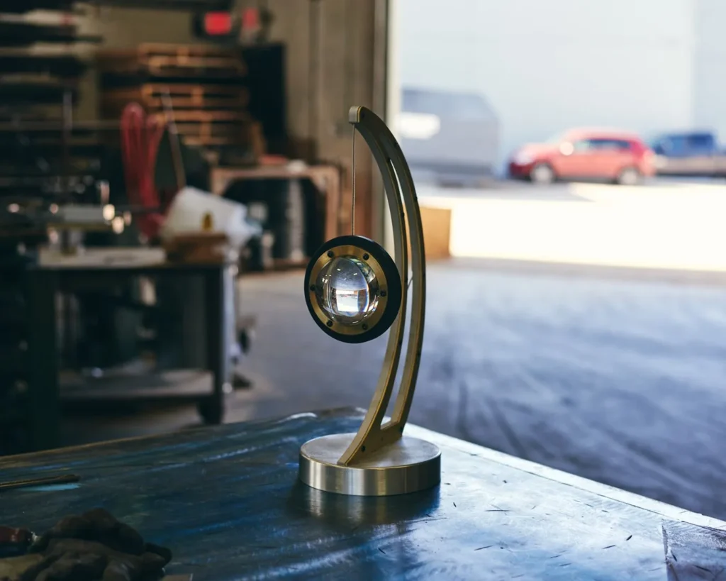 Da Vinci Infinity 1519 table lamp with setting-sun form, genuine brass details, and suspended illuminated capsule. Designed and manufactured by Karice.