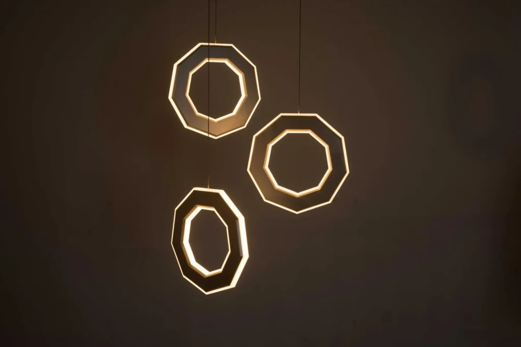 Ennea LED pendant with illuminated inner and outer geometric rings, concealed wiring, and suspended aluminum frame. Designed and manufactured by Karice.
